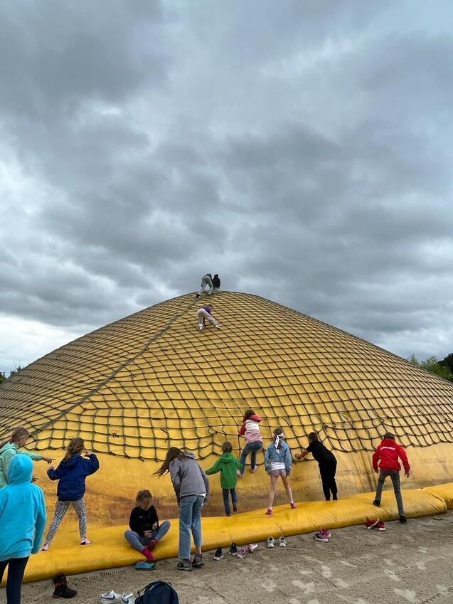 Kinder klettern auf eine gro&szlig;e, gelbe aufblasbare Kuppel unter einem bew&ouml;lkten Himmel.