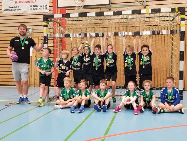 Gruppe von Kindern in Sportkleidung mit Medaillen, posierend vor einem Handballtor in einer Sporthalle.