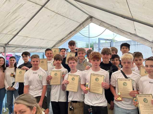Gruppe von Jugendlichen mit Urkunden und Medaillen in einem Zelt bei einer Preisverleihung.