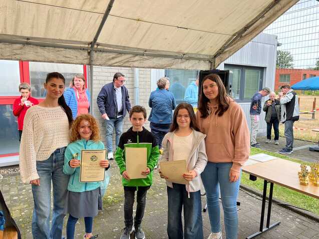 Sechs Kinder und Jugendliche stehen unter einem Zelt, halten Urkunden und lächeln in die Kamera. Hintergrund mit Zuschauern.