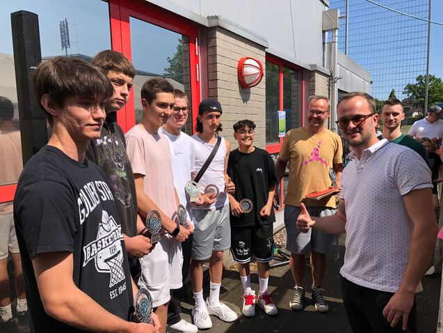 Gruppenfoto von jungen M&auml;nnern mit Medaillen, stehen vor einem Geb&auml;ude. Ein Mann sch&uuml;ttelt einem anderen die Hand.