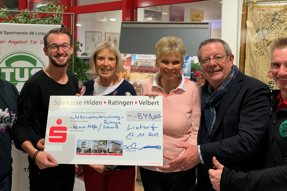 Gruppenszene mit Menschen, die einen gro&szlig;en Scheck &uuml;ber 8.490 Euro in der Hand halten, vor einer Tischtennisplatte.