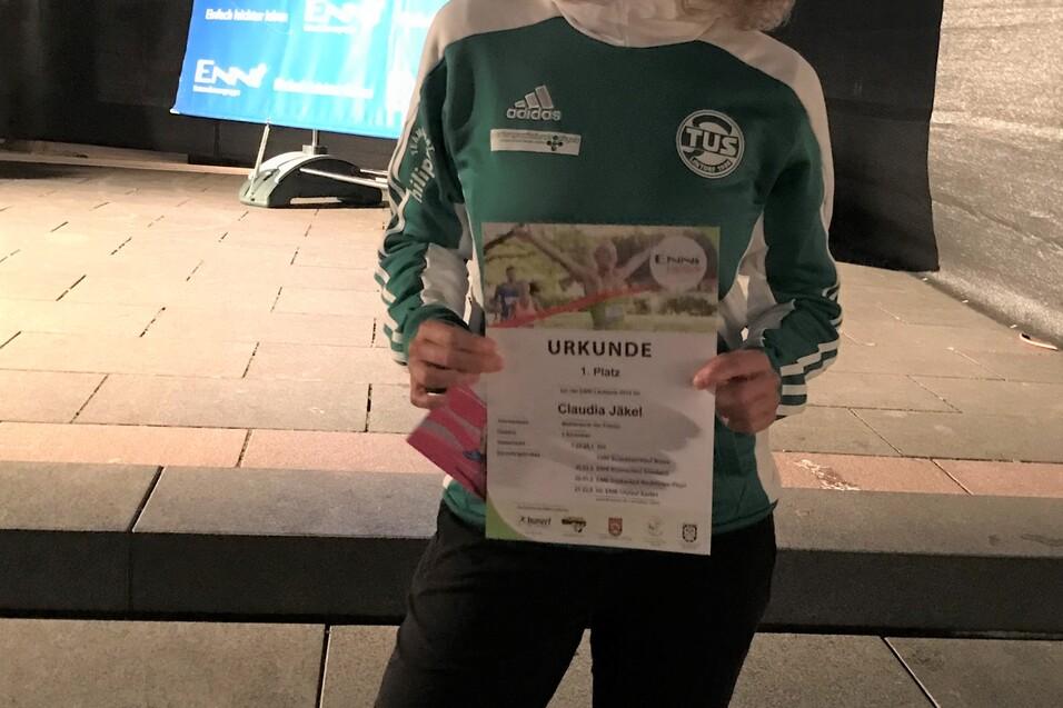 Frau mit sportlicher Kleidung h&auml;lt eine Urkunde f&uuml;r den ersten Platz auf einer Veranstaltung im Freien.