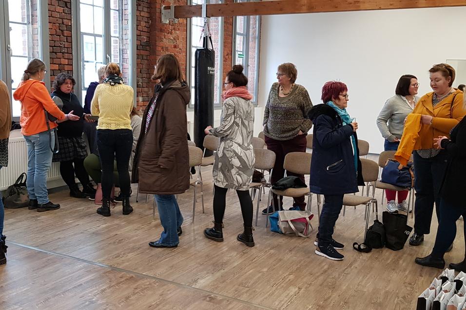 Gruppenszene in einem hellen Raum, Frauen stehen und unterhalten sich, einige sitzen auf St&uuml;hlen.