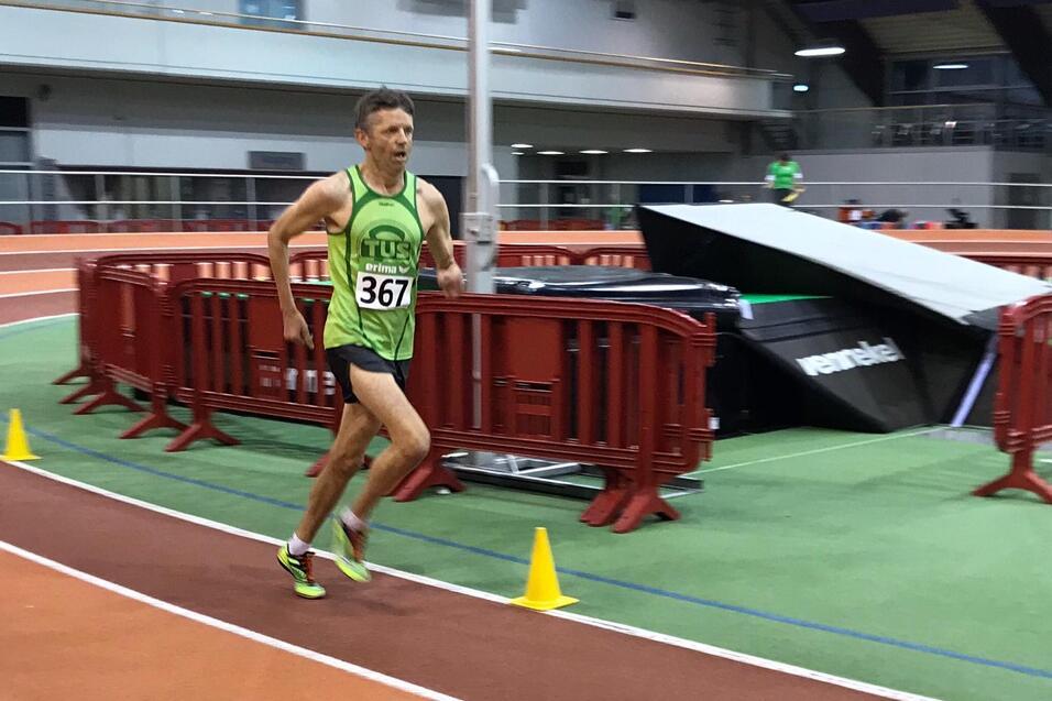 L&auml;ufer in gr&uuml;nem Trikot mit der Nummer 367 sprintet auf einer Indoor-Bahn mit roten Absperrungen und gelben Pylonen.