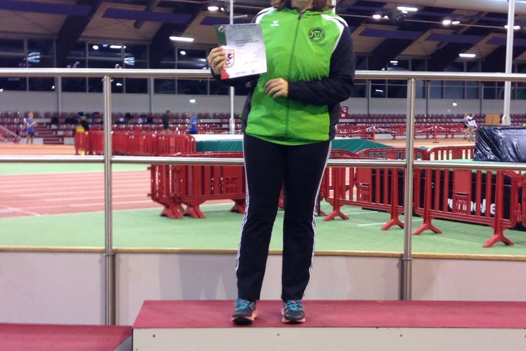 Sportlerin steht auf dem Siegertreppchen und h&auml;lt eine Urkunde in der Hand, Hintergrund einer Sporthalle.