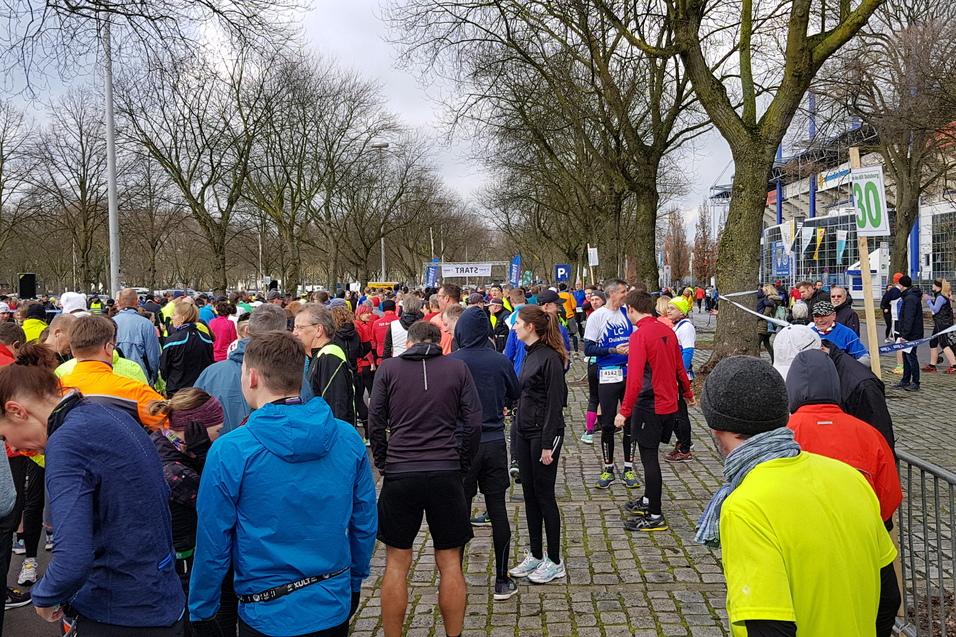 Gro&szlig;e Menschenmenge in Sportkleidung versammelt sich f&uuml;r ein Lauf-Event unter B&auml;umen an einem grauen Tag.