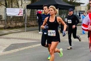 L&auml;uferinnen und L&auml;ufer absolvieren ein Stra&szlig;enrennen, w&auml;hrend im Hintergrund ein Zelt und Zuschauer zu sehen sind.