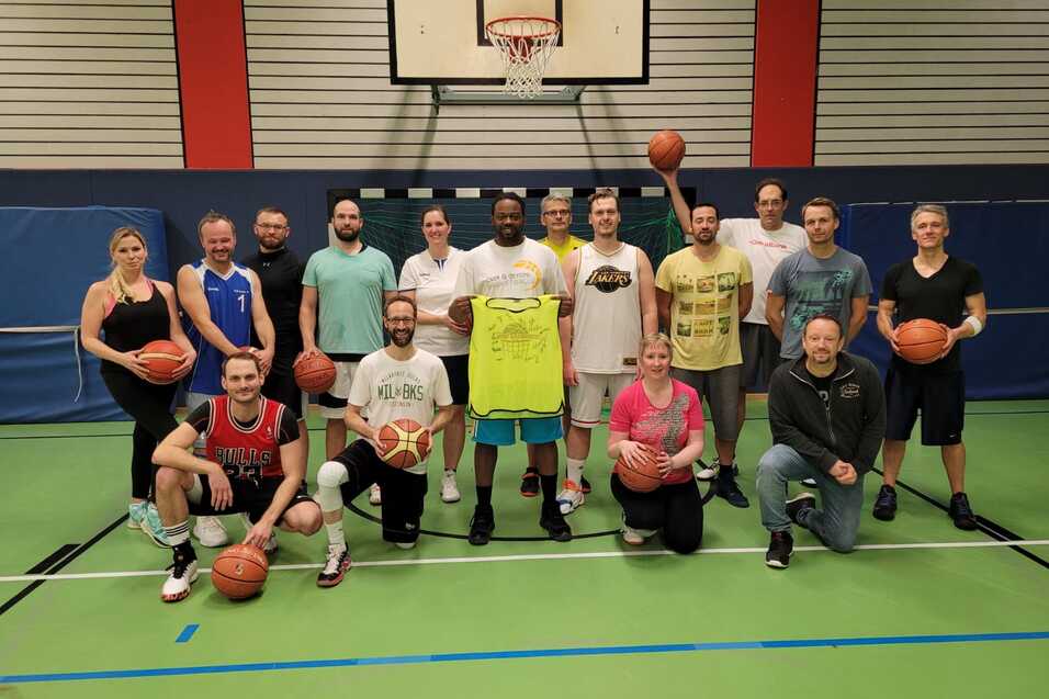 Gruppe von 20 Basketballspielern in Sportkleidung, stehend auf dem Feld mit Basketballs in der Hand, vor dem Korb.