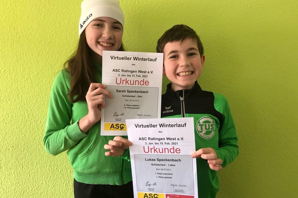 Zwei Kinder halten Urkunden des ASC Ratingen West e.V. f&uuml;r den virtuellen Winterlauf vor einer gr&uuml;nen Wand.