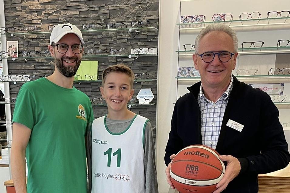 Drei Personen l&auml;cheln in einem Brillengesch&auml;ft, einer h&auml;lt einen Basketball, w&auml;hrend die anderen im Sportoutfit sind.