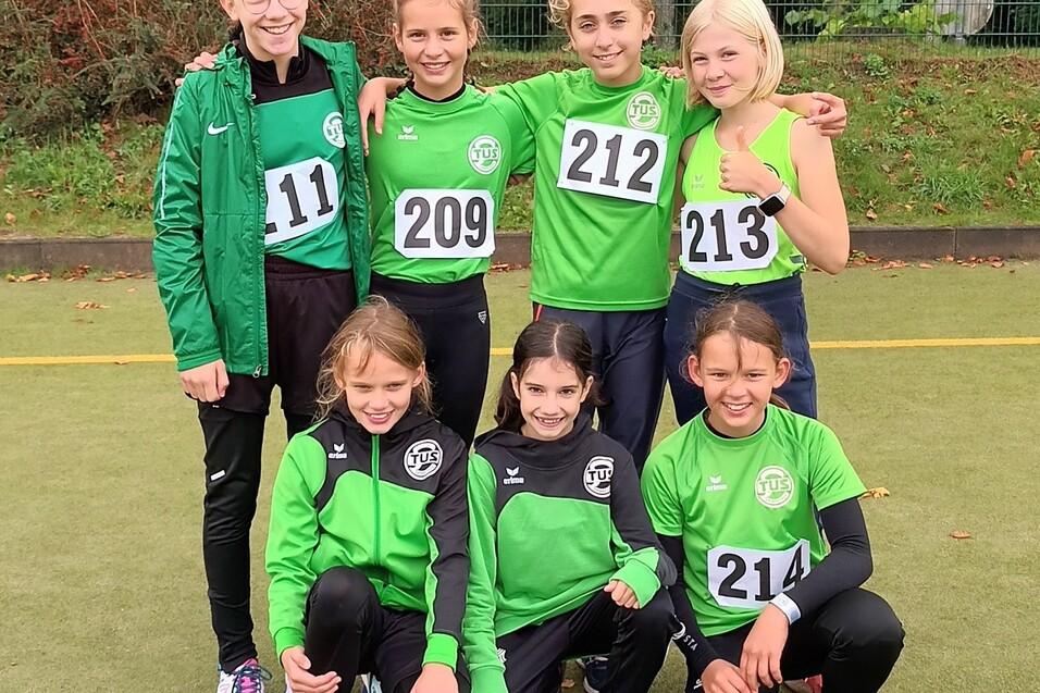 Gruppe von sieben M&auml;dchen in gr&uuml;nen Sportanz&uuml;gen, posierend auf einem Sportplatz.