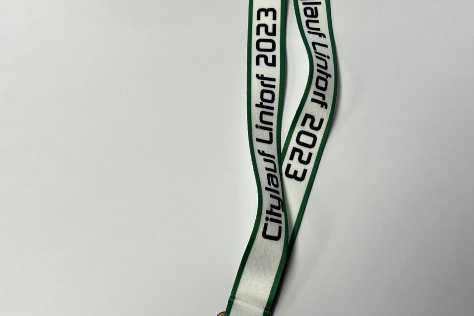 Holzmedaille mit gr&uuml;n-wei&szlig;em Band und Aufschrift &bdquo;Citylauf Linthorf 2023&ldquo; sowie Sportmotiven.