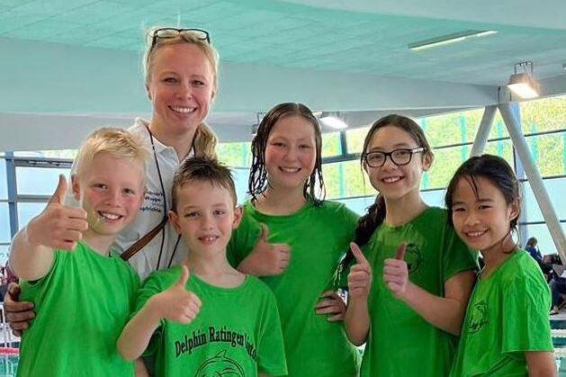 Gruppe von f&uuml;nf Kindern in gr&uuml;nen T-Shirts mit Daumen hoch, umgeben von einer Freibad-Umgebung.