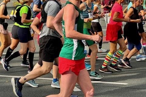 L&auml;uferin in gr&uuml;n-rotem Outfit joggt l&auml;chelnd auf einer belebten Stra&szlig;e w&auml;hrend eines Wettkampfs.