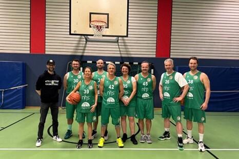 Gruppenfoto einer Basketballmannschaft in gr&uuml;nen Trikots, posierend auf einem Basketballfeld mit Korb im Hintergrund.