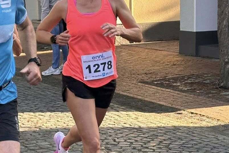 Frau in pinkem Sporttop läuft auf einem Kopfsteinpflasterweg, während ein Mann neben ihr läuft. Teilnehmernummer 1278 sichtbar.