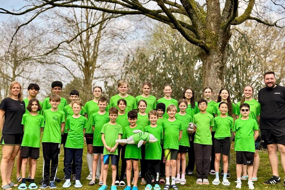 Gruppe von Jugendlichen und Trainern in gr&uuml;nen T-Shirts steht unter einem Baum auf einer Wiese.