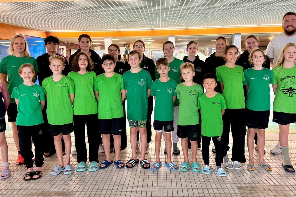 Gruppenshot von Schwimmern in gr&uuml;nen Shirts vor einem Schwimmbecken, begleitet von Trainern und Betreuern.