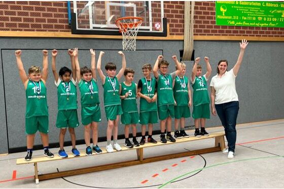 Gruppe von zehn Jungen in gr&uuml;nen Basketballtrikots mit Medaillen, posierend auf einer Plattform, umgeben von Begeisterung.