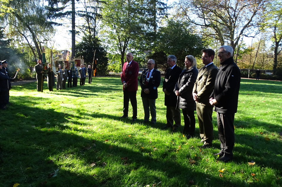 Gruppenbild von f&uuml;nf Personen, die an einer Gedenkfeier im Freien teilnehmen; im Hintergrund eine Ehrenwache.