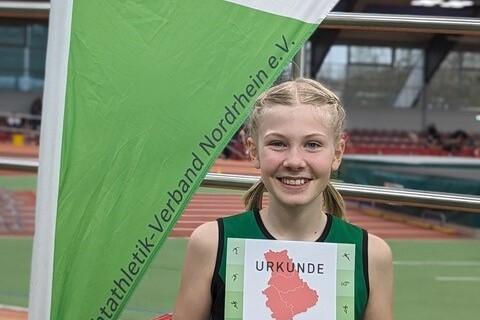 L&auml;chelndes M&auml;dchen in gr&uuml;ner Sportbekleidung h&auml;lt eine Urkunde des LV Nordrhein vor einem Veranstaltungsbanner.