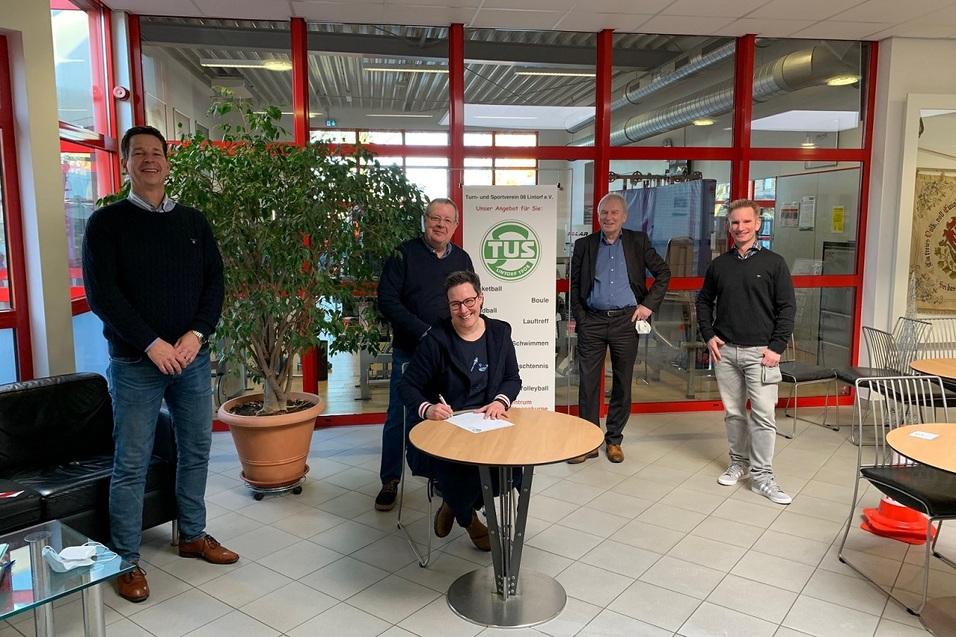 F&uuml;nf M&auml;nner stehen um einen Tisch, w&auml;hrend einer von ihnen etwas auf ein Dokument unterschreibt.