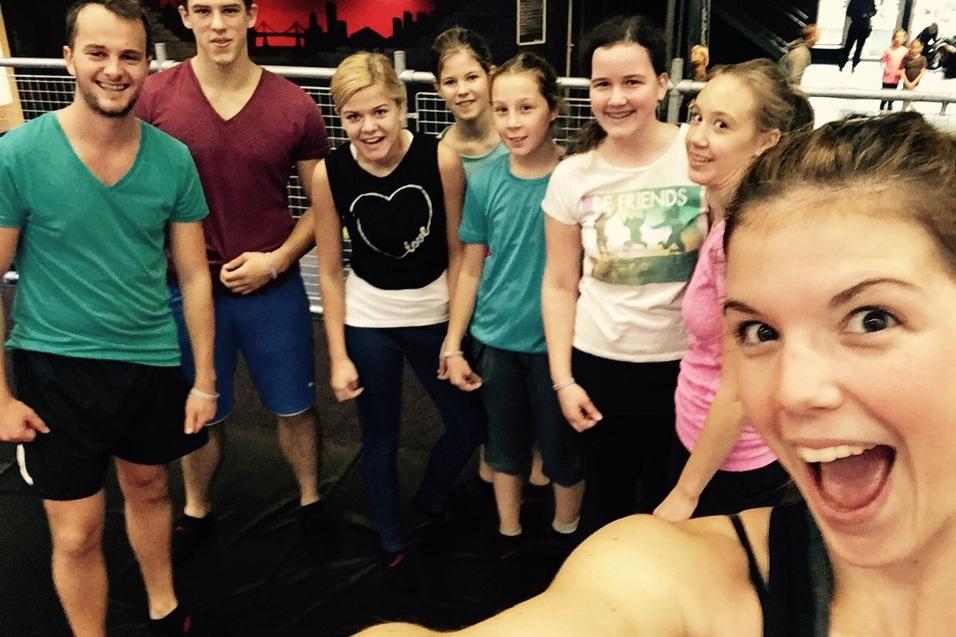 Gruppe junger Menschen posiert beim Gruppenfoto in einem Sportstudio mit L&auml;cheln und aktiver K&ouml;rperhaltung.