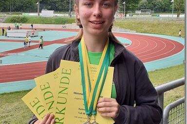 Ein l&auml;chelndes M&auml;dchen h&auml;lt mehrere Sporturkunden und Medaillen in der Hand, mit einem Sportplatz im Hintergrund.