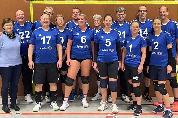 Gruppe von Volleyballspielern in blauen Trikots mit der Aufschrift "Apollo" steht lächelnd in einer Sporthalle.