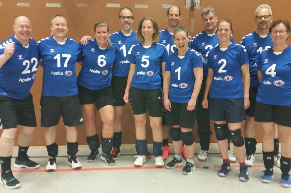 Mannschaftsfoto von zw&ouml;lf Handballspielern in blauen Trikots, l&auml;chelnd in einer Sporthalle aufgestellt.
