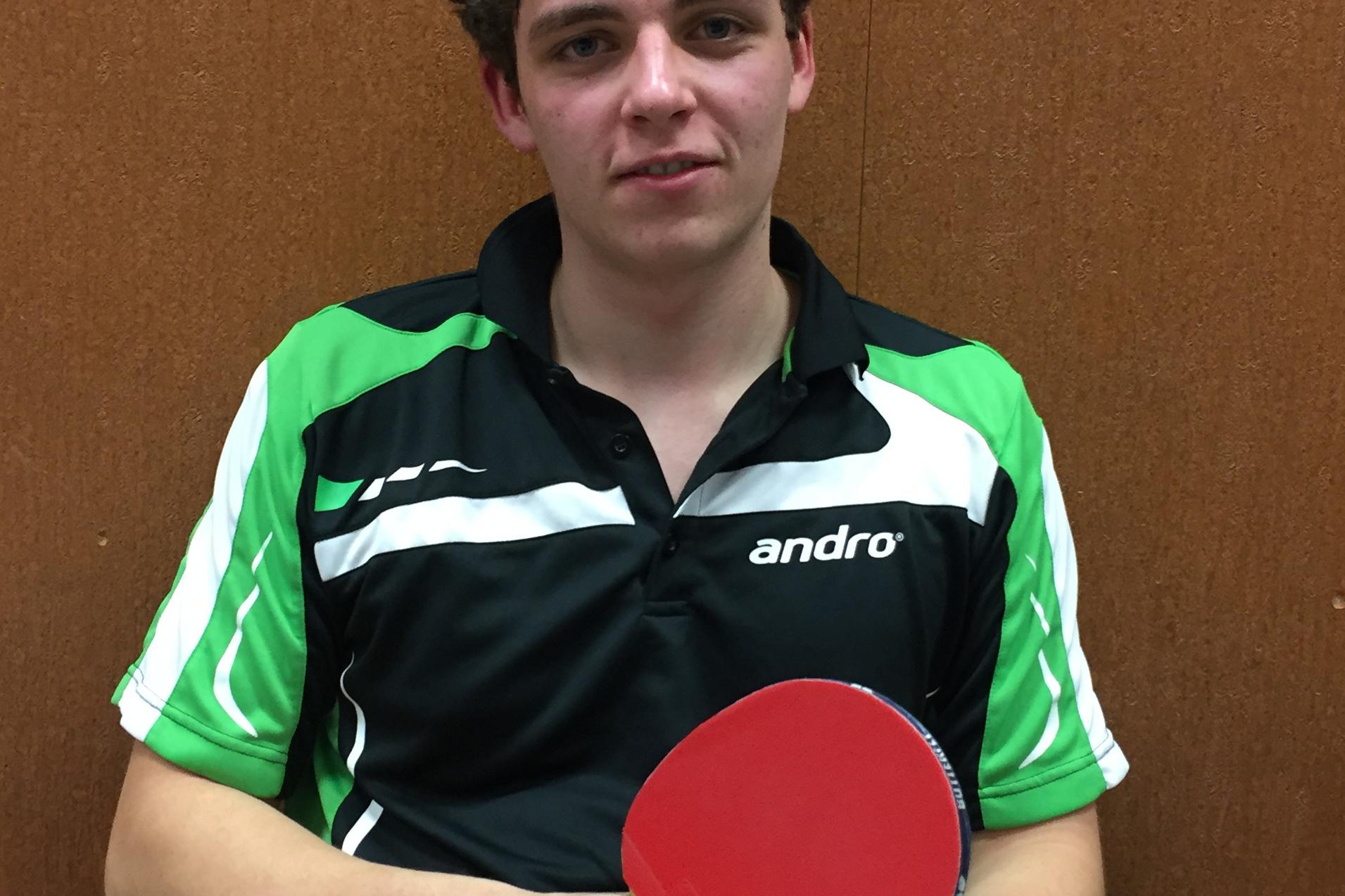 Junger Mann im Tischtennistrikot h&auml;lt einen Tischtennisschl&auml;ger und sitzt auf der Bank neben einem Handtuch.