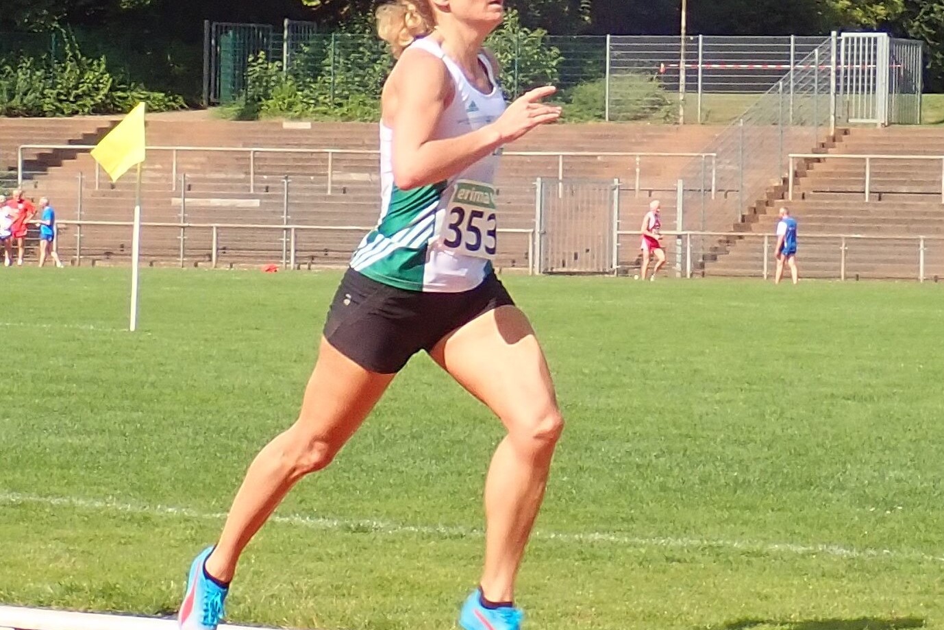 Athletin mit Startnummer 353 l&auml;uft energisch auf einer Laufbahn, im Hintergrund sind Zuschauer und Trib&uuml;nen sichtbar.