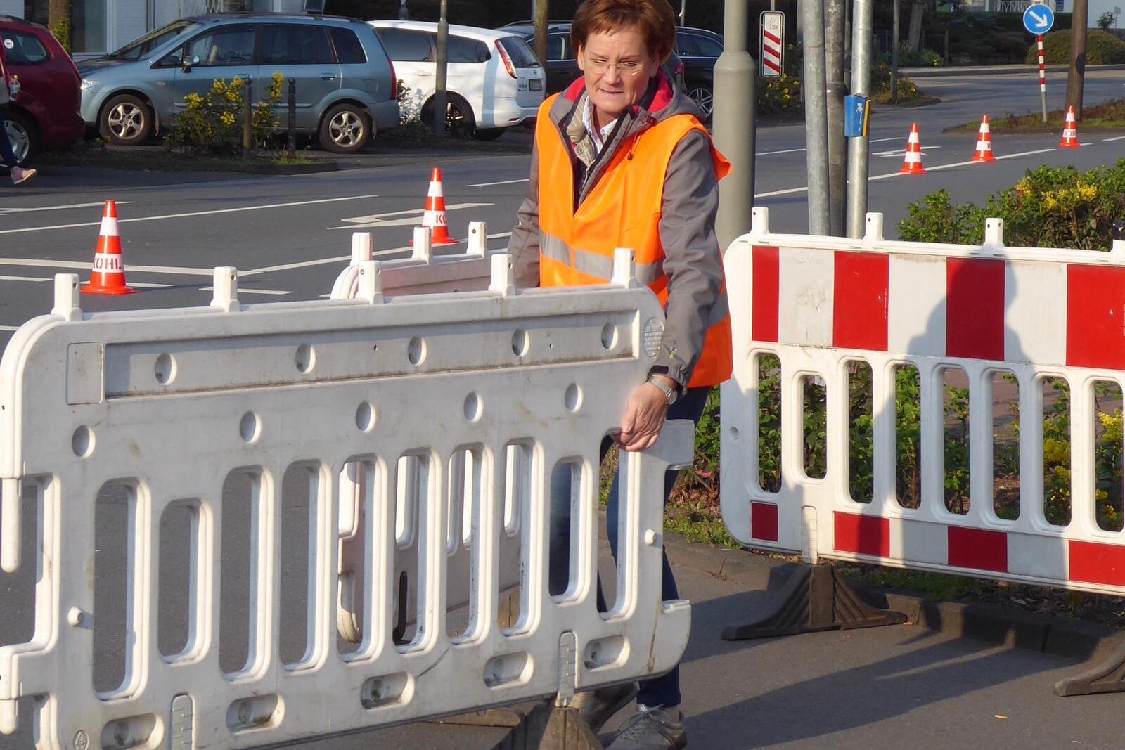 Frau in orangefarbener Warnweste stellt eine Verkehrsabsperrung auf einer Straße in der Stadt auf.