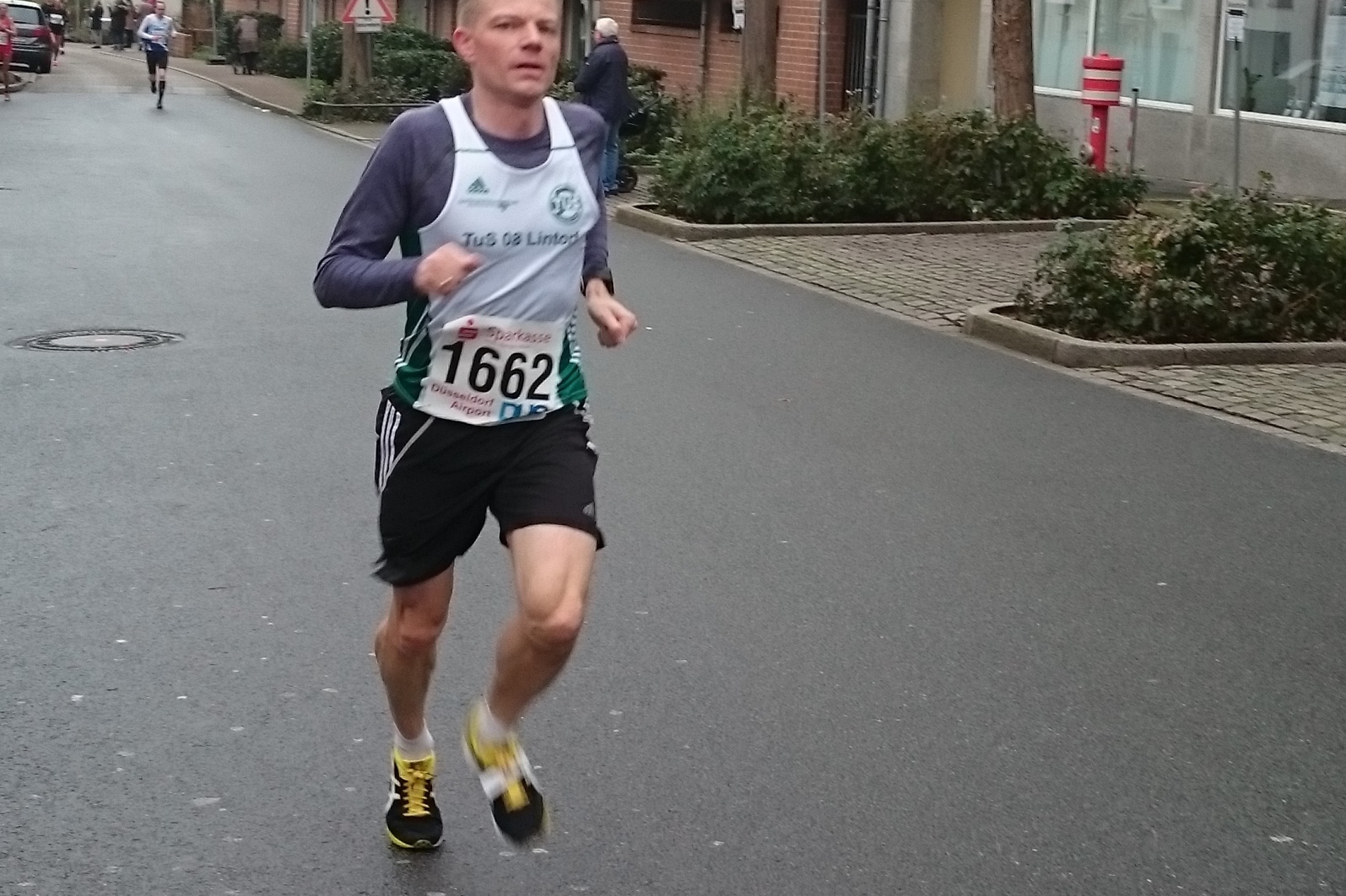 L&auml;ufer mit Startnummer 1662 joggt auf einer Stra&szlig;enstra&szlig;e zwischen Geb&auml;uden w&auml;hrend eines Wettkampfs.