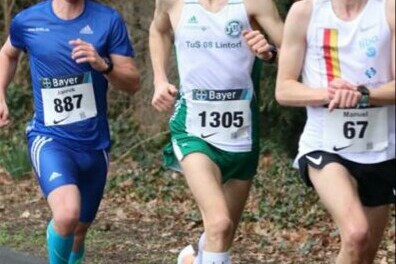 Drei L&auml;ufer in Wettkampfbekleidung laufen auf einer Stra&szlig;e entlang, umgeben von B&auml;umen. Die Nummern 887, 1305 und 67 sind sichtbar.