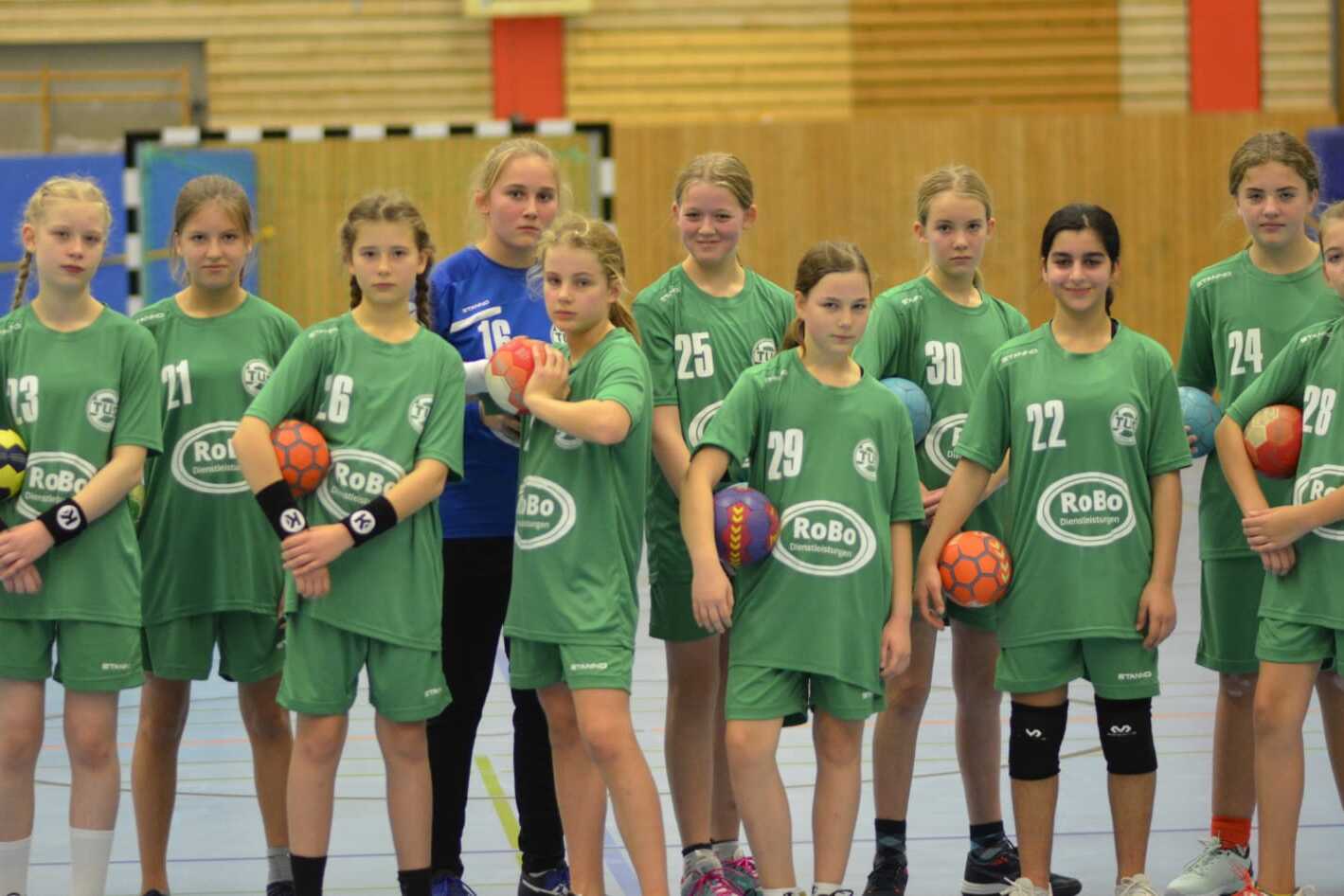 Mannschaftsfoto eines Handballteams mit jungen Spielerinnen in gr&uuml;nen Trikots, die B&auml;lle in H&auml;nden halten.
