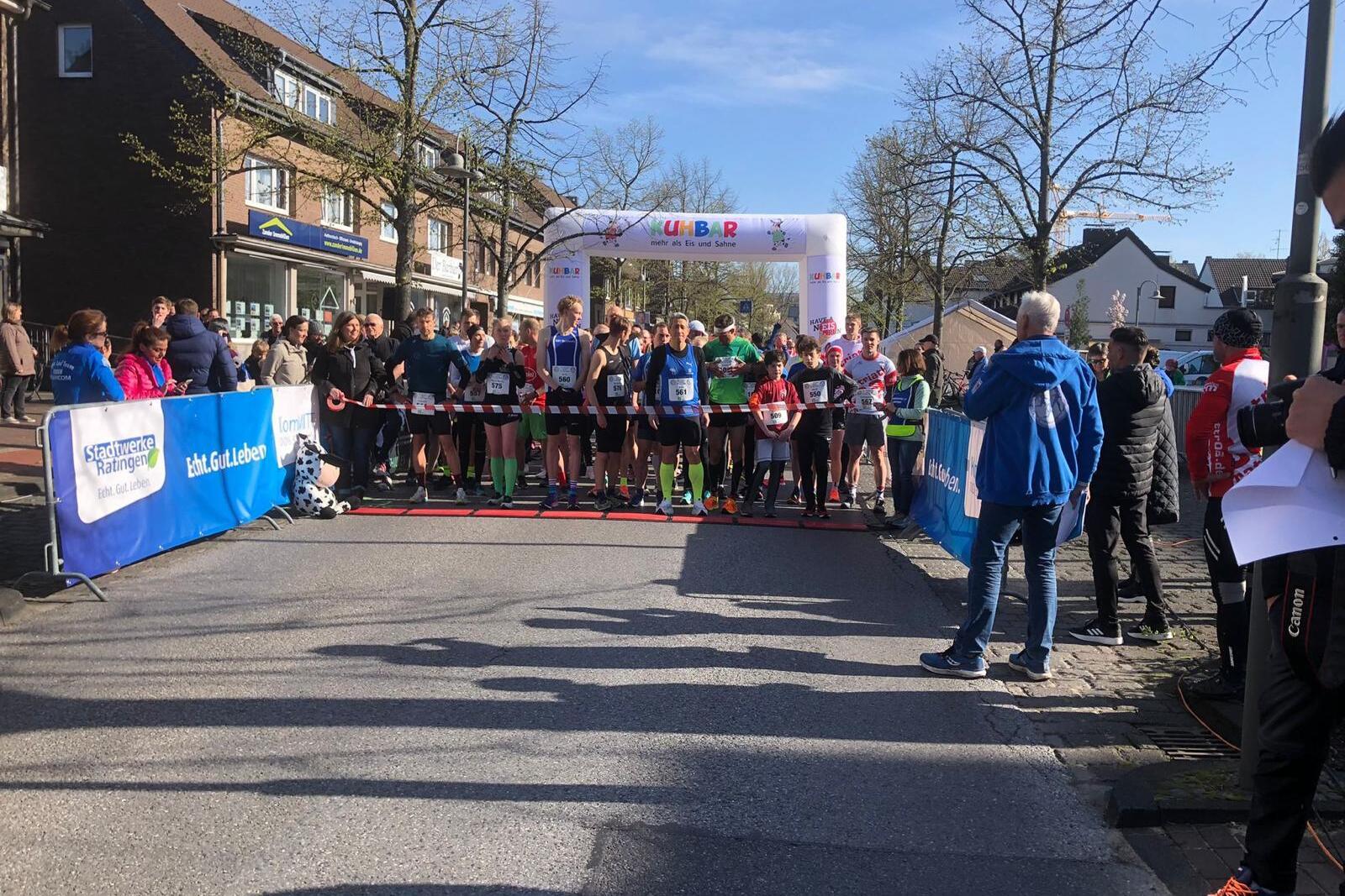 Startlinie eines Laufwettbewerbs mit Teilnehmern, Zuschauern und einem Bogen im Hintergrund.