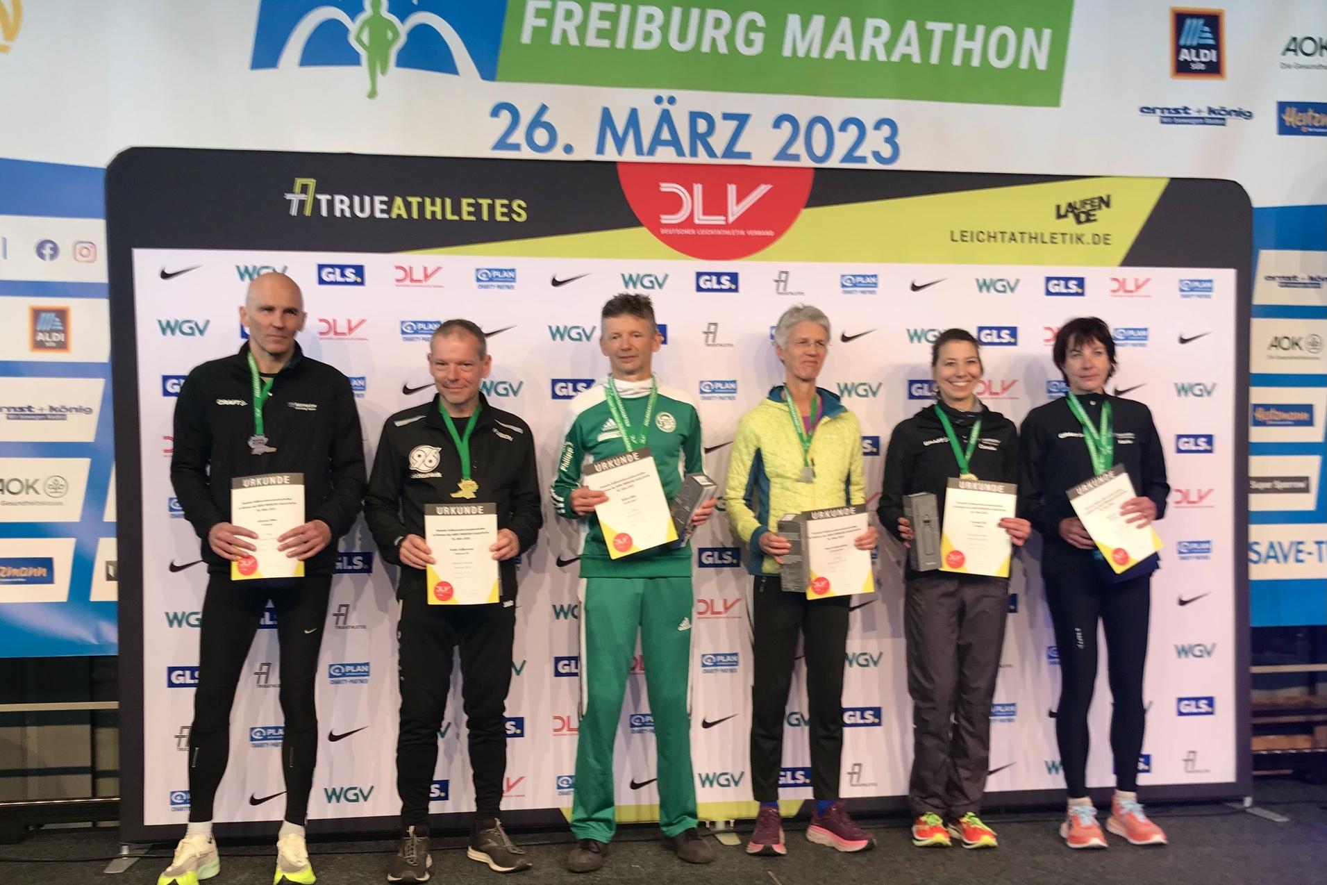 Sechs Personen mit Medaillen und Urkunden stehen auf einer B&uuml;hne beim Freiburg Marathon am 26. M&auml;rz 2023.