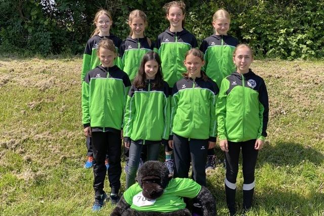 Gruppenshooting von neun Mädchen in grünen Sportjacken, umgeben von Natur, mit einem großen Stoffgorilla im Vordergrund.