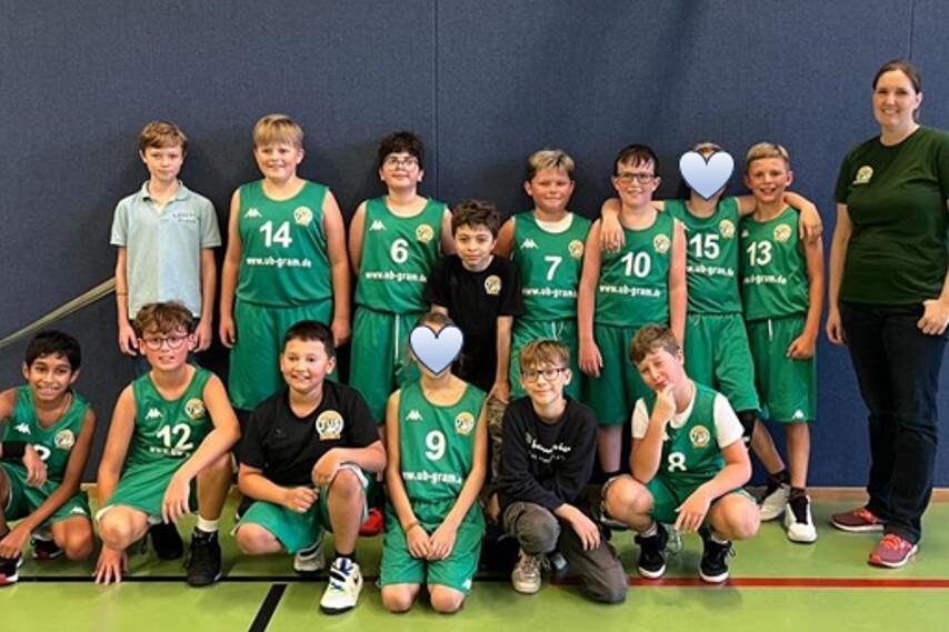 Gruppe von Basketballspielern in gr&uuml;nen Trikots, aufgestellt vor einer Wand in einer Sporthalle.