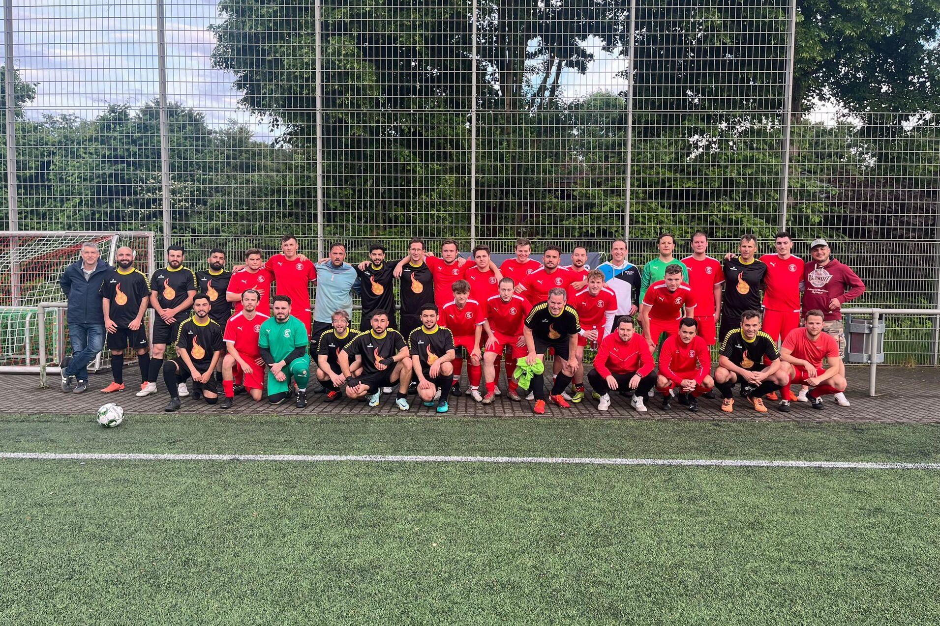 Gruppenfoto von Spielern in schwarzen und roten Trikots, die auf einem Fu&szlig;ballplatz posieren.