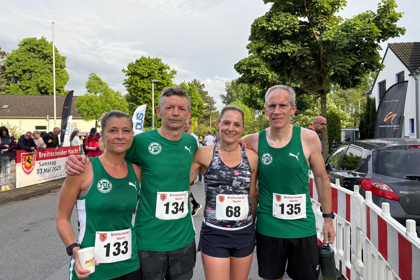 Vier L&auml;ufer in gr&uuml;nen Trikots stehen gemeinsam an einem Laufstartpunkt, bereit f&uuml;r einen Wettkampf.