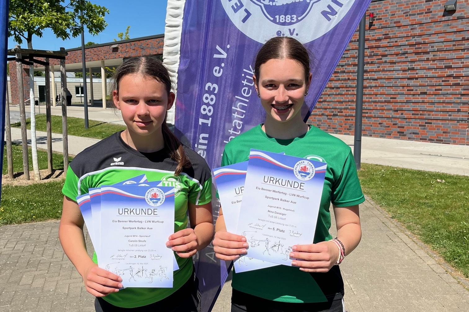 Zwei M&auml;dchen halten stolz ihre Urkunden vor einem Banner des TV Eichlingern im Freien.