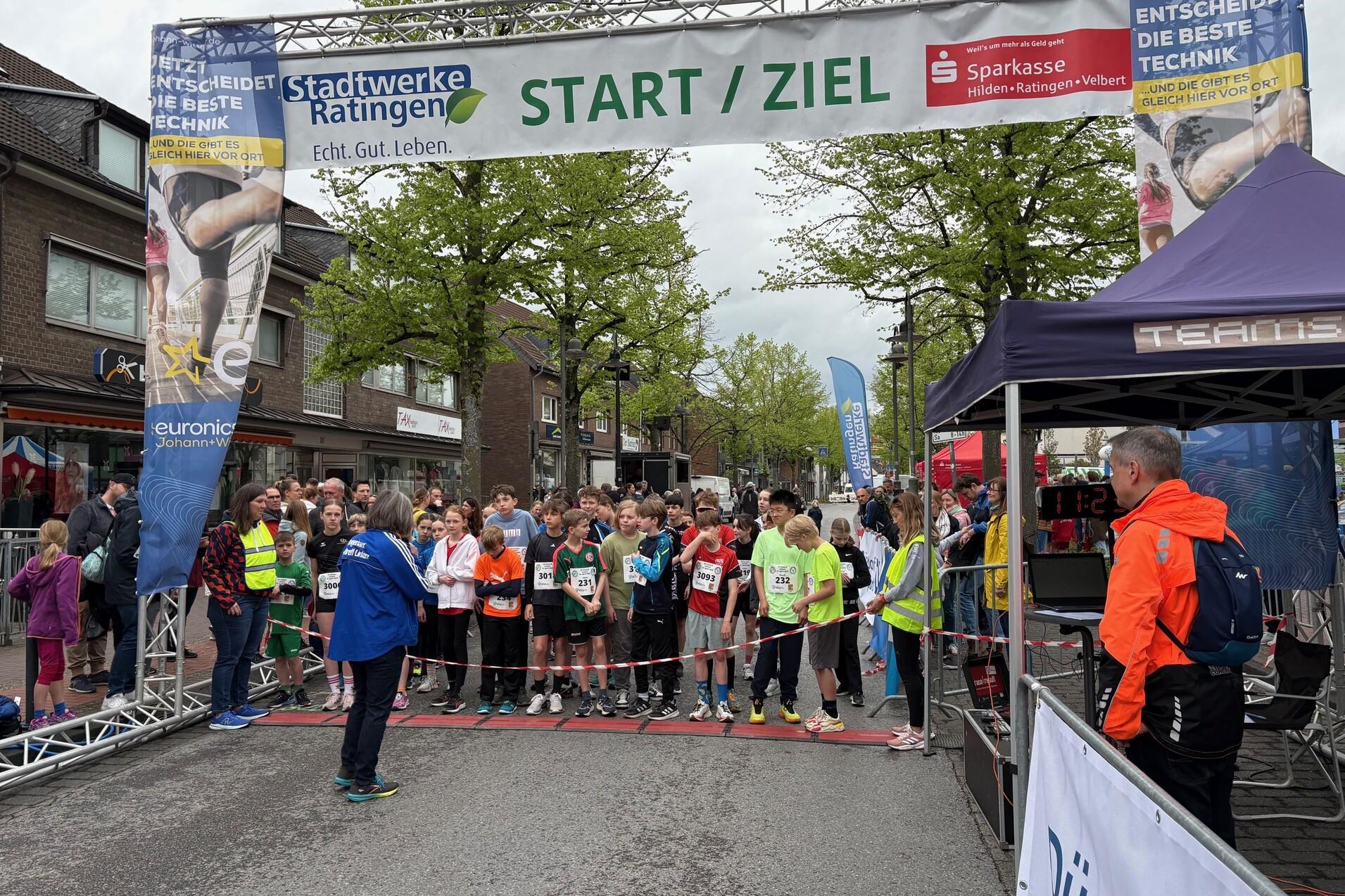 Startlinie eines Laufwettbewerbs mit wartenden Teilnehmern und Zuschauern unter einem großen Banner „START / ZIEL“.