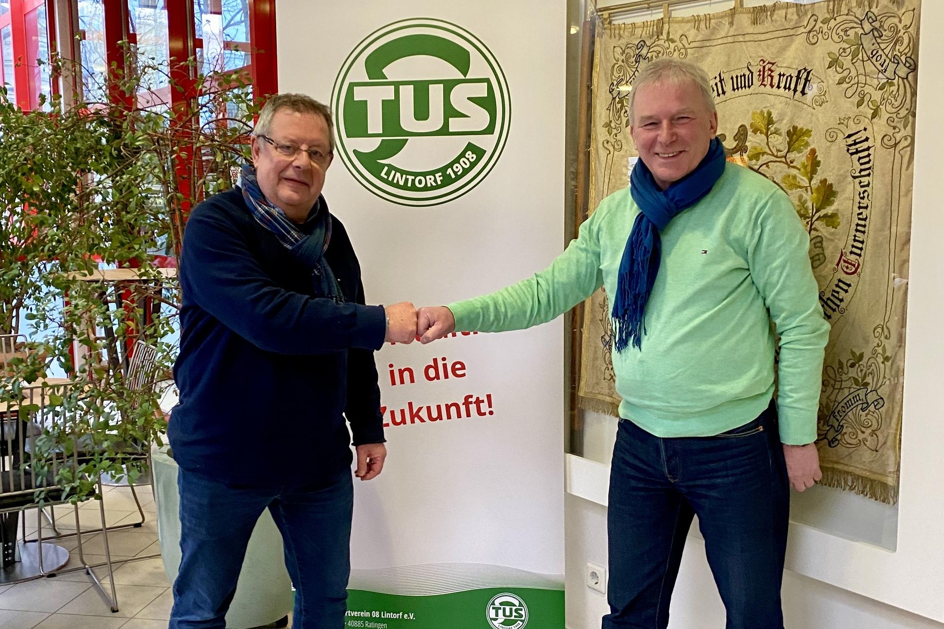 Zwei M&auml;nner sch&uuml;tteln sich die H&auml;nde vor einem Banner der TUS Lintorf in einem hellen Raum mit Pflanzen.