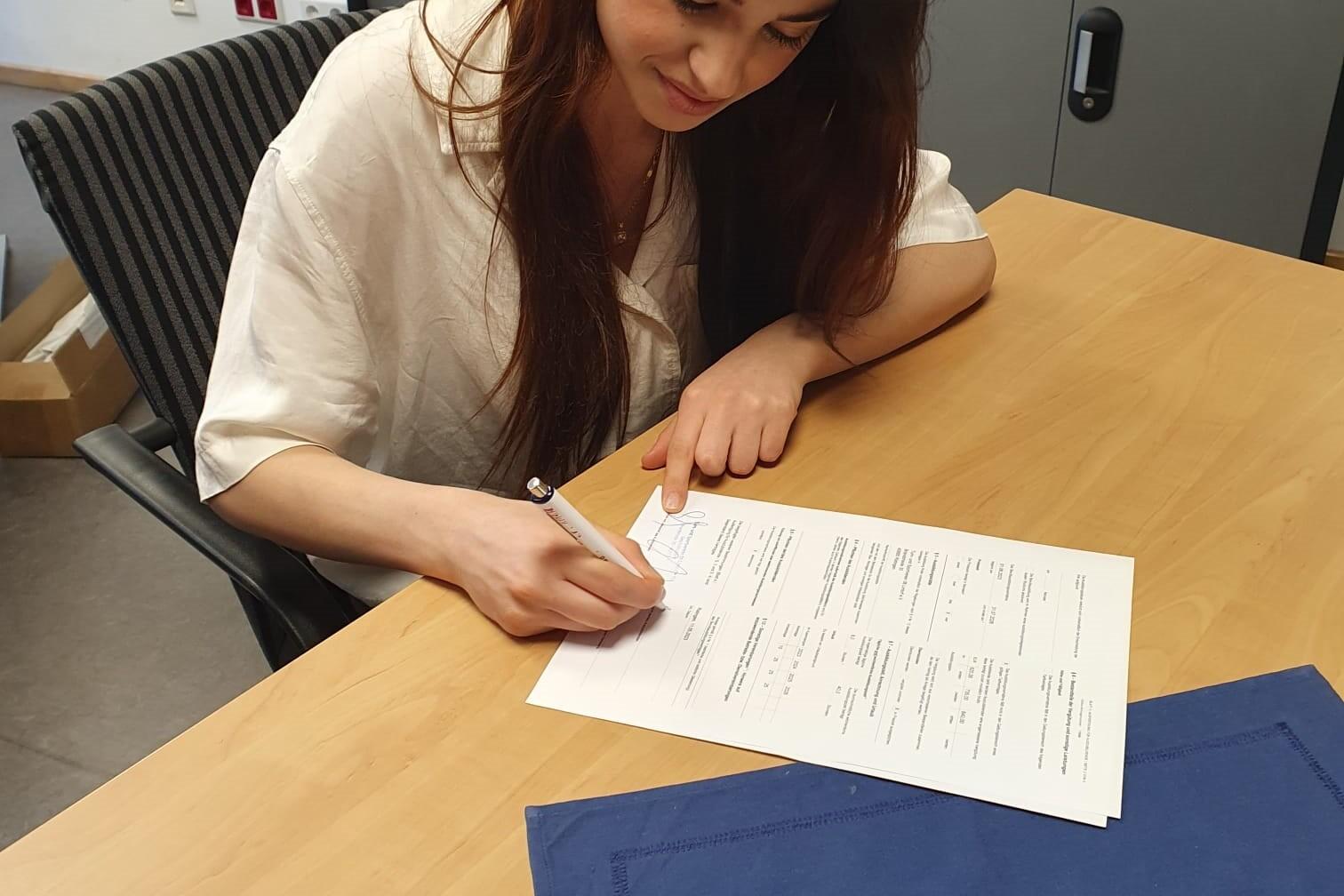 Junge Frau schreibt konzentriert auf einem Dokument an einem Tisch in einem Büro.