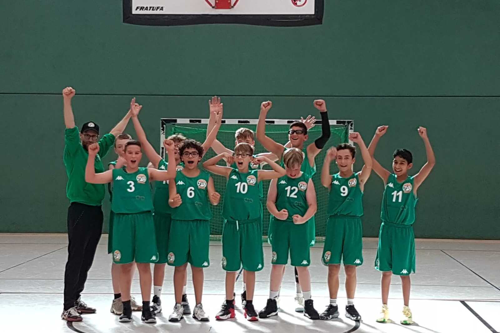 Gruppennaufnahme von Basketballspielern in gr&uuml;nen Trikots, die jubelnd auf dem Spielfeld stehen.