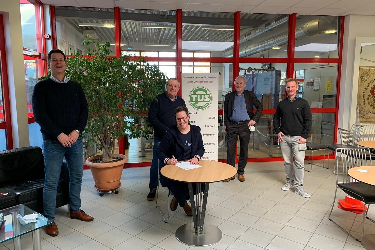 F&uuml;nf M&auml;nner stehen um einen Tisch, w&auml;hrend einer von ihnen etwas auf ein Dokument unterschreibt.