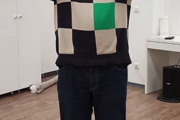 Mann mit buntem Pulli h&auml;lt einen Pokal &uuml;ber seinem Kopf in einem hellen Raum.